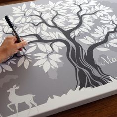 a person is writing on a large canvas with a tree and deer painted on it