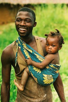 a man carrying a baby in a sling on his back and smiling at the camera