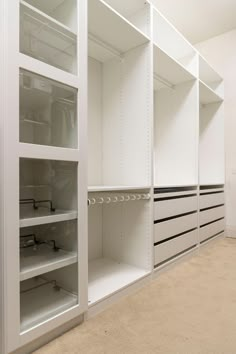 an empty walk in closet with lots of white shelves and shelving unit doors open