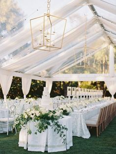 an outdoor tent with tables and chairs covered in white linens, flowers and greenery