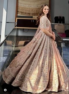 a woman in a pink and gold gown is standing on the stairs with her hands behind her back