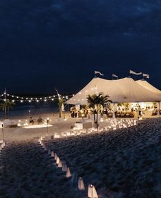 a large tent set up on the beach at night with lit candles and palm trees