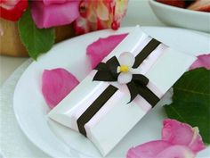 a white plate topped with a piece of cake next to pink roses and a bowl of fruit