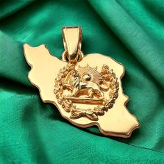 a gold pendant with the state of south africa on it's side, sitting on a green satin background