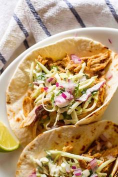 three tacos on a plate with cole slaw and lime