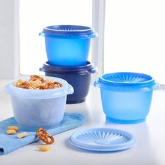 three plastic containers with lids and some pretzels in front of them on a table