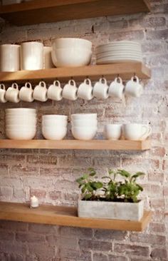 the shelves are filled with white dishes and cups on wooden shelves next to a brick wall