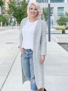 a woman standing on the sidewalk wearing jeans and a cardigan