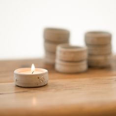 a lit candle sitting on top of a wooden table next to stacks of coins in the background