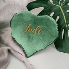 a green heart shaped pillow with the word jade on it next to a monster leaf