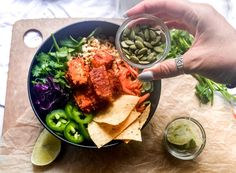 a person holding a bowl filled with vegetables and tortilla chips on top of a cutting board