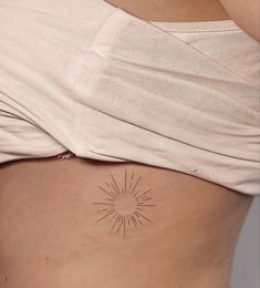 a woman's stomach with a small sun tattoo on the side of her belly