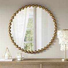 a round mirror sitting on top of a wooden dresser next to a vase and lamp