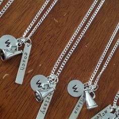 four personalized necklaces with bells on them sitting on a wooden table, one has a name tag and the other has a bell