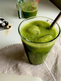 a green drink in a glass on a table with two spoons next to it