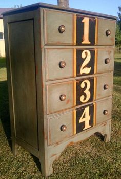 an old dresser with numbers on it in the grass near a house and trees,