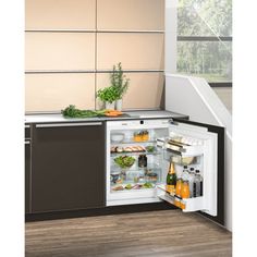 an open refrigerator in a kitchen next to a stair case with vegetables and drinks on it