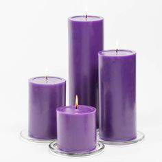 three purple candles sitting next to each other on a glass plate with one candle lit