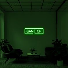 a green neon sign that says game on in front of a dark room with two chairs and a coffee table