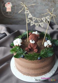 a teddy bear on top of a cake decorated with greenery and cotton garlands