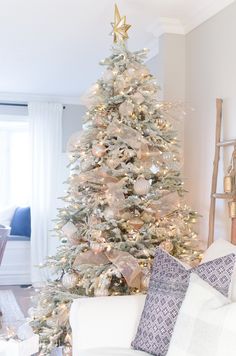 a white christmas tree in a living room with gold and silver ornaments on the top