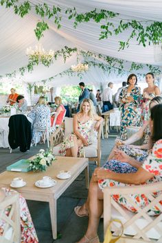 a group of women sitting in chairs under a tent next to tables with plates and cups on them