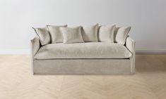 a couch with pillows on top of it in front of a white wall and wooden floor