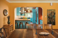 an open kitchen and dining room area with wood table, blue cabinets and yellow walls