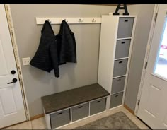 a coat rack with two coats hanging on it next to a door and some drawers