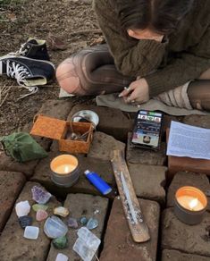 a woman sitting on the ground next to some rocks and candles