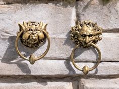 two brass lion head door handles on a stone wall, one has a ring handle and the other has a face