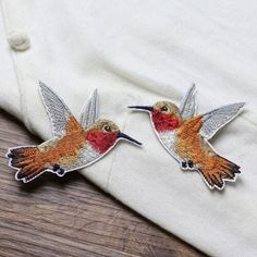 two embroidered hummingbirds sitting on top of a white shirt