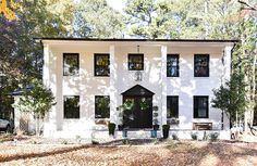 a white house with black shutters and trees in the background