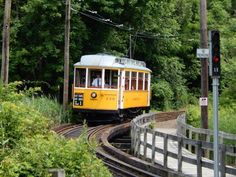 a yellow trolley car traveling down tracks next to trees