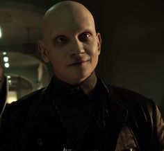 a bald man in a black shirt and leather jacket looking at the camera with an evil look on his face