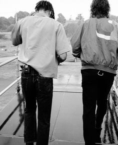 two people walking on a bridge in the rain with their backs to each other and one person holding an umbrella