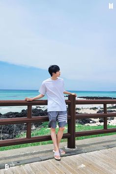 a man standing on top of a wooden deck next to the ocean with his hands on his hips