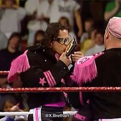 two men standing next to each other in front of a wrestling ring with pink and black outfits