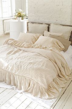 a bed with ruffled sheets and pillows in a room next to a brick wall