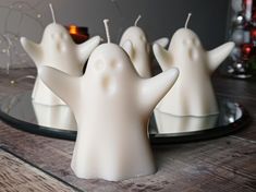 some white candles sitting on top of a wooden table next to a plate with ghost candles