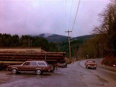 two cars are parked on the side of the road in front of a large pile of logs