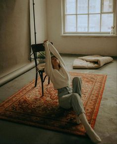 a woman sitting on top of a rug in front of a window with her arms up