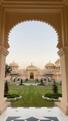 an archway leading to a large building in the middle of a green lawn with trees and bushes