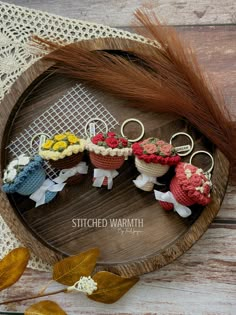 small knitted baskets with flowers are sitting on a wooden tray next to some leaves