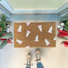 a person standing in front of a door mat with christmas trees on it and other decorations