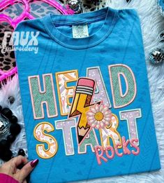 a blue shirt that says head start rocks with a pencil and flower on the front