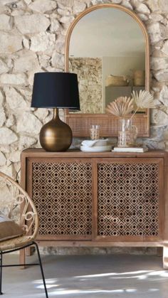 a wooden cabinet sitting next to a lamp on top of a table in front of a stone wall