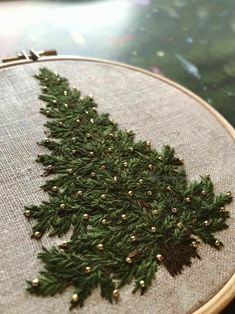 an embroidered christmas tree ornament is shown in the hoop with gold beading