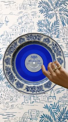 a person holding a blue and white plate in front of a wallpapered background