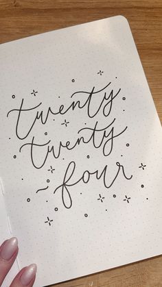 a hand holding a pen and writing on a notebook with the words twenty twenty four